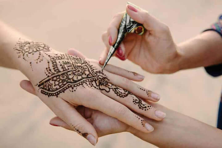 Intricate Moroccan henna design being applied to a hand using a henna cone.