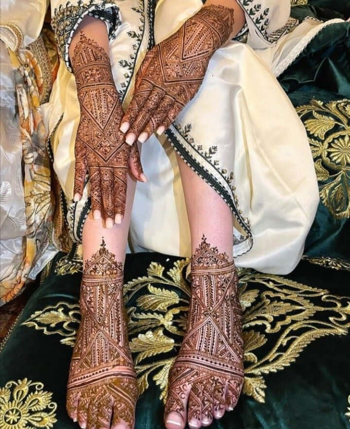 Intricate henna designs on hands and feet, showcasing traditional Moroccan art, with detailed patterns on a decorative fabric background.