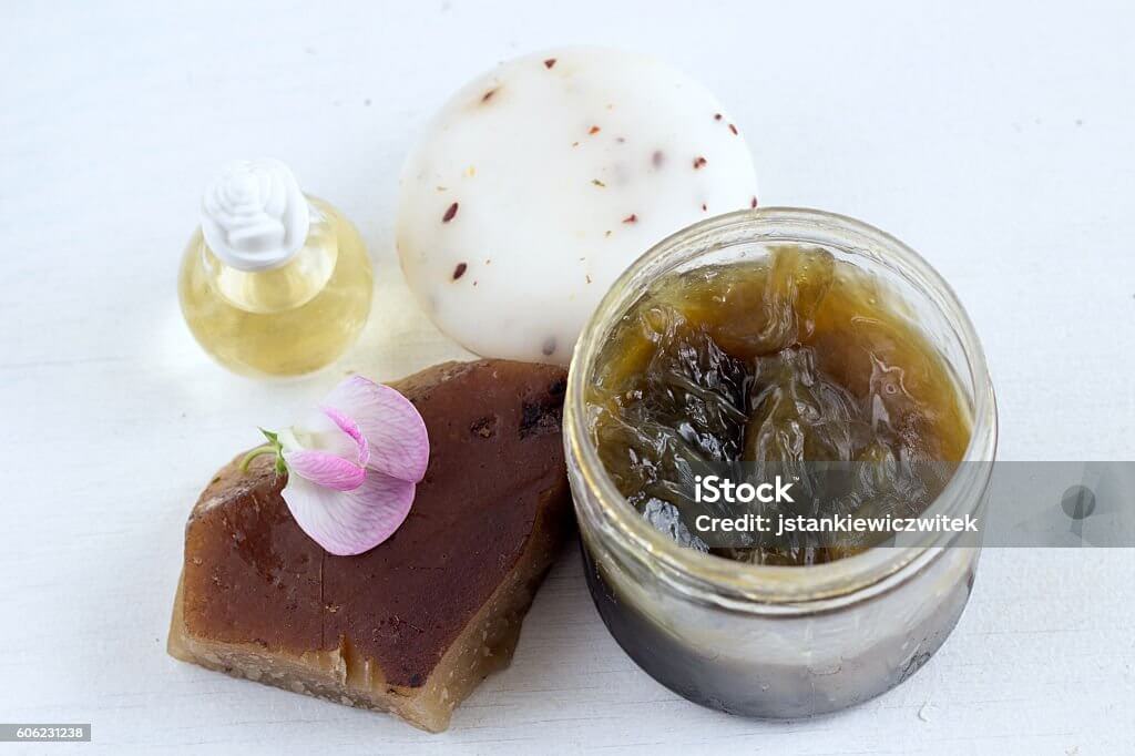 Moroccan black soap with Blue Nila in a jar, scrub glove, and essential oil bottle for detoxifying skincare.