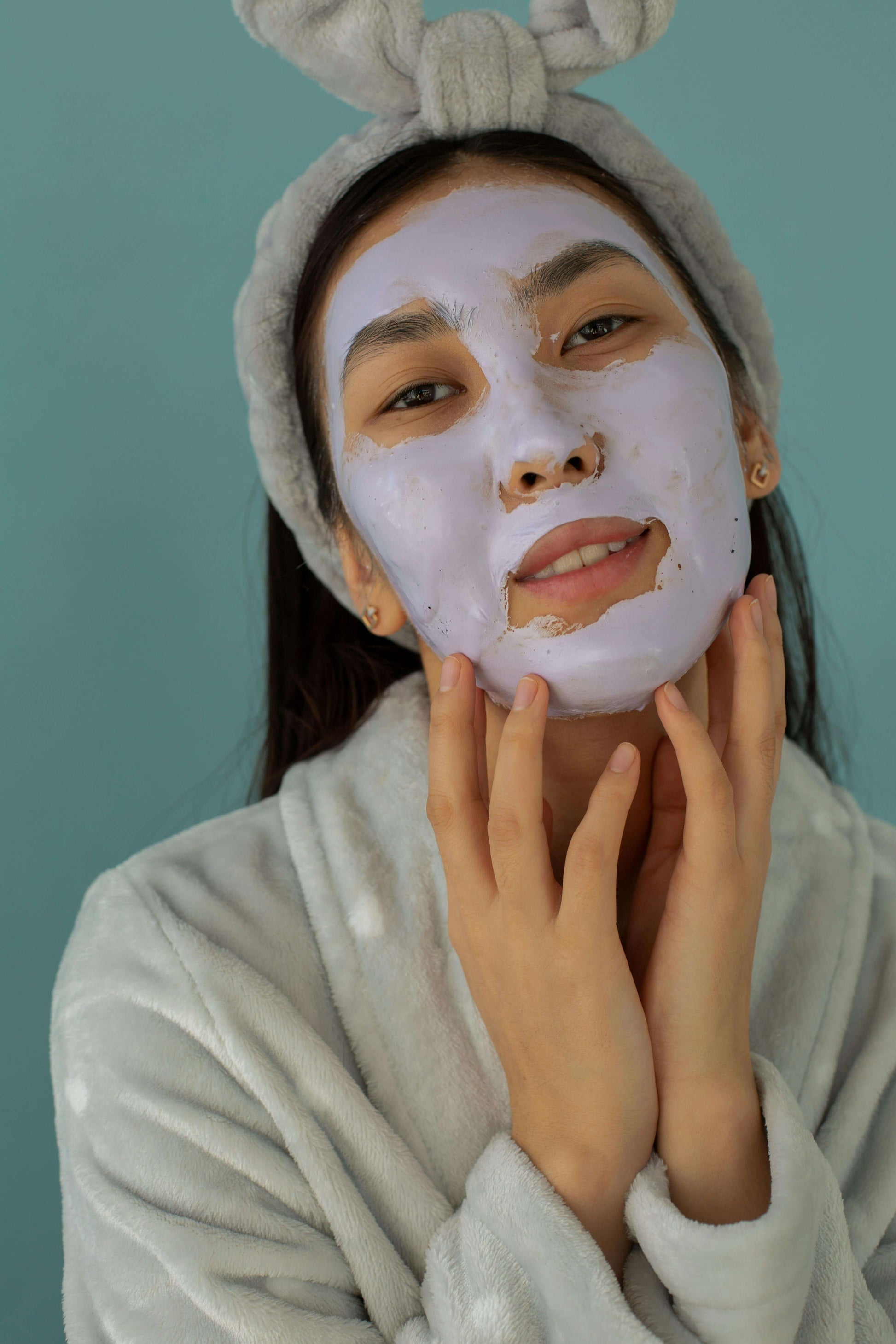 Woman wearing a gray headband applies a hydrating argan oil face mask for skincare treatment.