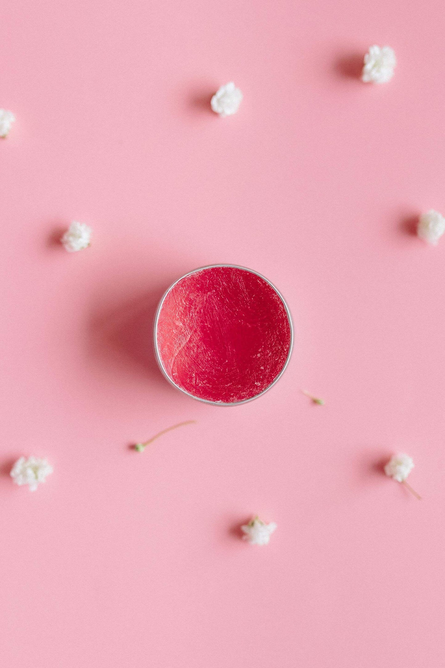 Pink lip balm in a round container on a pink background with white flowers scattered around.